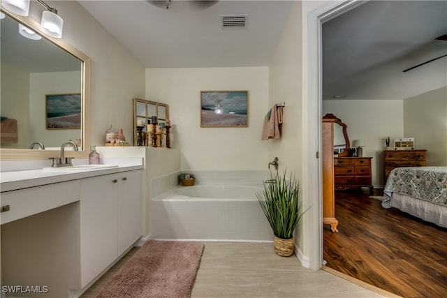 bathroom with hardwood / wood-style flooring, tiled bath, and vanity