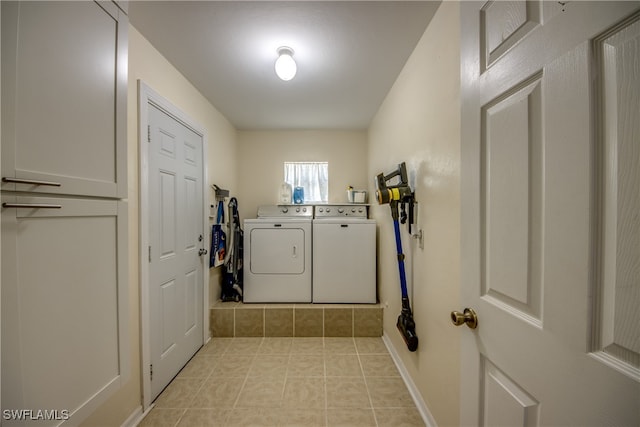 clothes washing area featuring washer and clothes dryer, light tile patterned flooring, and cabinets