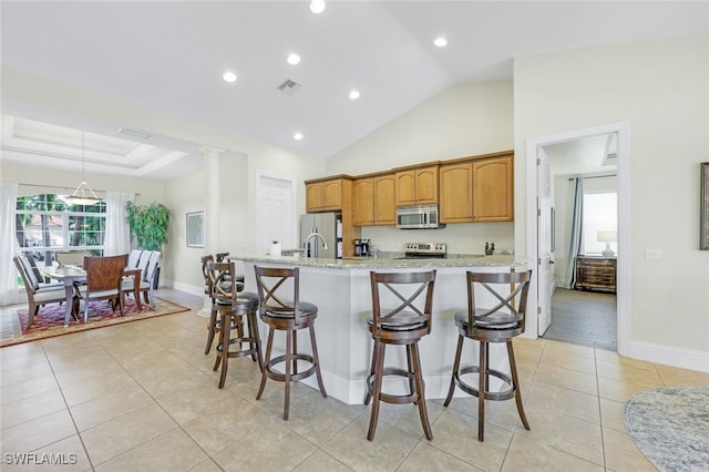 kitchen featuring decorative columns, a kitchen island with sink, stainless steel appliances, and a breakfast bar