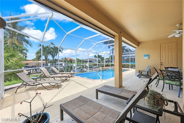 view of pool with a water view, glass enclosure, ceiling fan, and a patio area