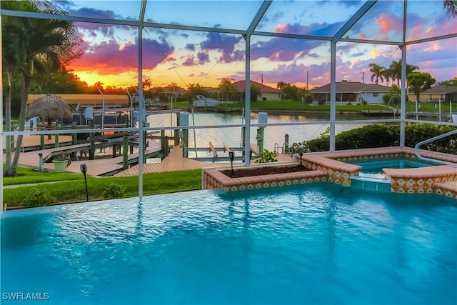 pool at dusk with glass enclosure, a boat dock, a water view, and an in ground hot tub