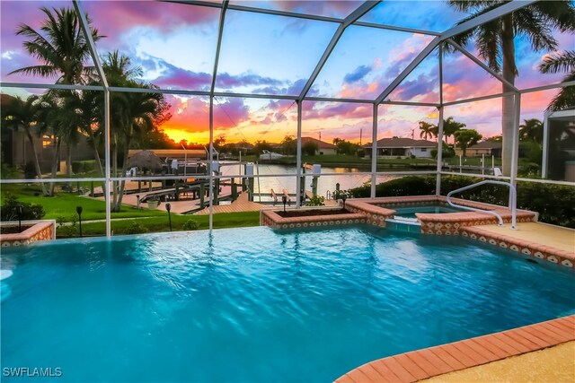 pool at dusk with a lanai, a water view, and an in ground hot tub