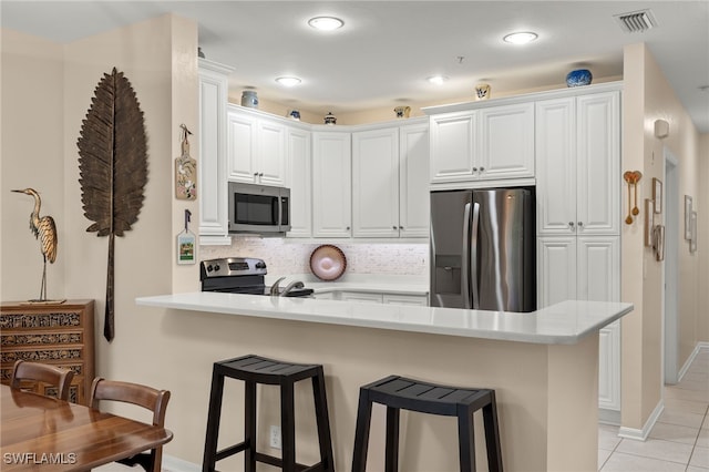 kitchen with kitchen peninsula, backsplash, appliances with stainless steel finishes, a breakfast bar, and white cabinetry