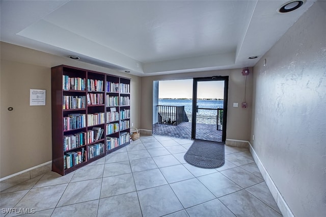 tiled spare room featuring a tray ceiling and a water view