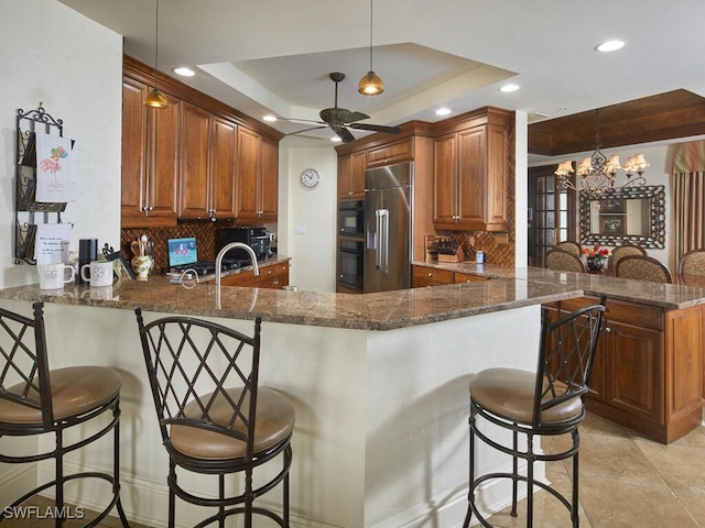 kitchen with high quality fridge, kitchen peninsula, pendant lighting, and a raised ceiling