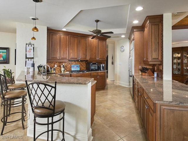 kitchen featuring a raised ceiling, decorative light fixtures, kitchen peninsula, and a kitchen breakfast bar