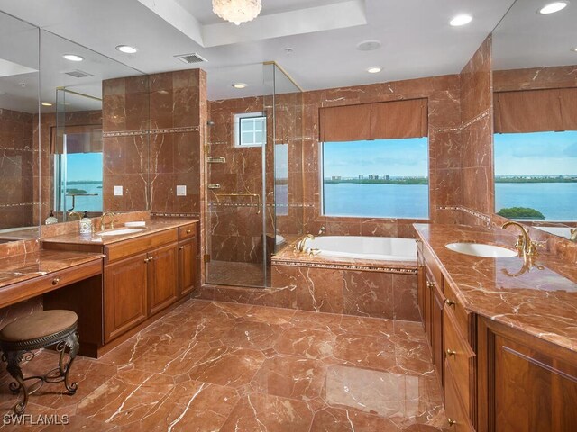 bathroom with plus walk in shower, a tray ceiling, vanity, tile walls, and a water view