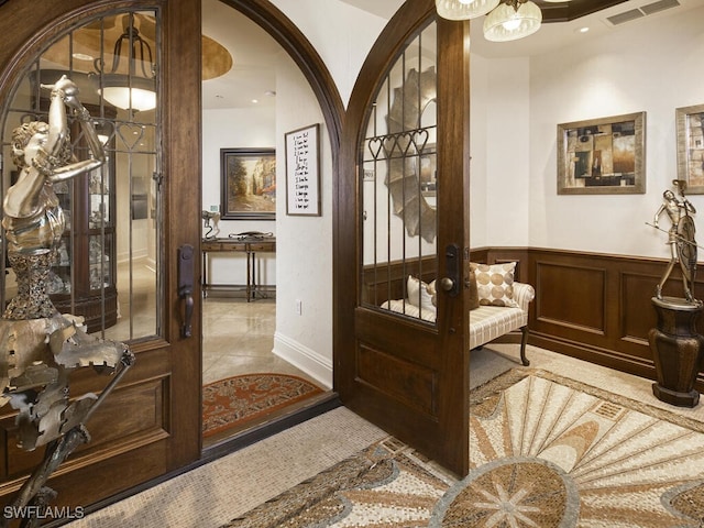 interior space with visible vents, tile patterned floors, a wainscoted wall, french doors, and arched walkways