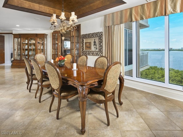 dining area featuring a water view, an inviting chandelier, and a raised ceiling