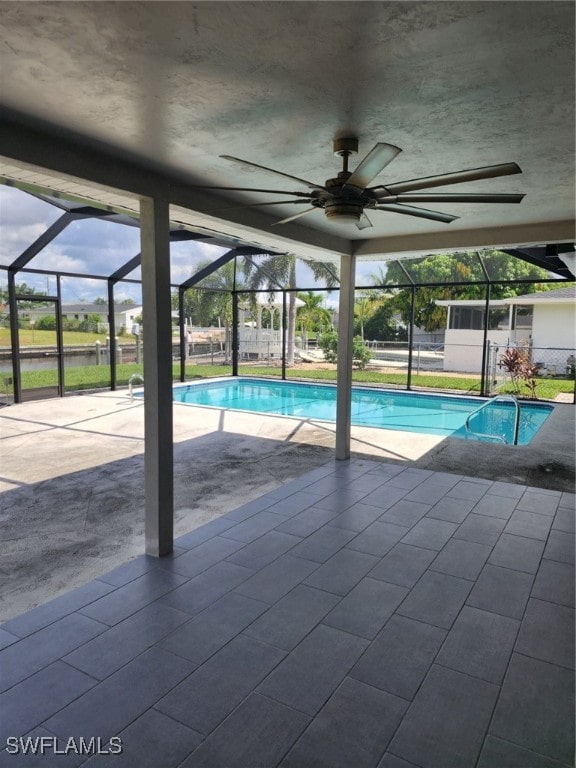 view of swimming pool with glass enclosure, ceiling fan, and a patio area