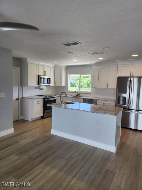 kitchen with white cabinets, appliances with stainless steel finishes, a center island, light stone countertops, and dark hardwood / wood-style flooring