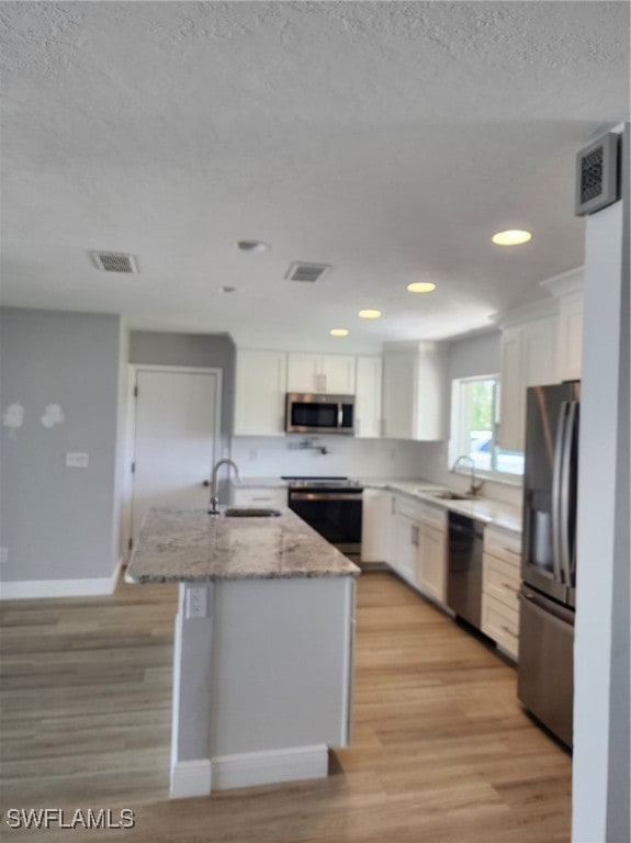 kitchen featuring light hardwood / wood-style flooring, white cabinetry, appliances with stainless steel finishes, a center island, and light stone countertops