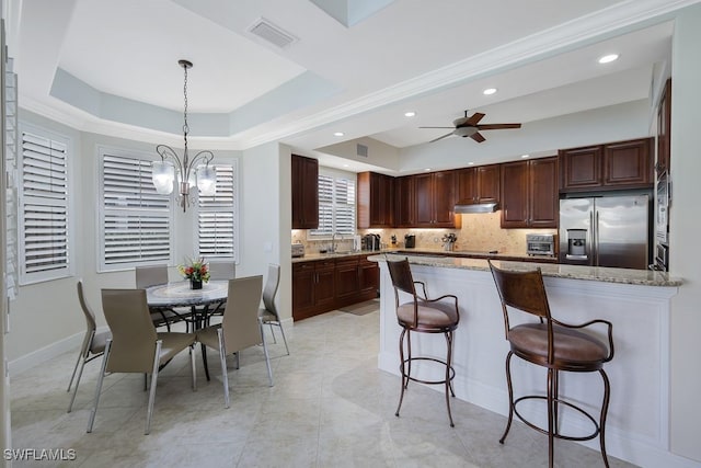 kitchen with a raised ceiling, visible vents, stainless steel fridge, a peninsula, and a kitchen bar