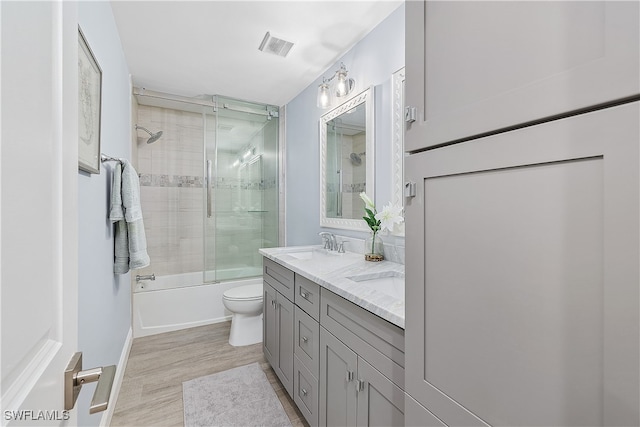 full bathroom with combined bath / shower with glass door, vanity, toilet, and hardwood / wood-style flooring