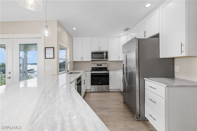 kitchen featuring sink, white cabinets, appliances with stainless steel finishes, decorative light fixtures, and light stone countertops