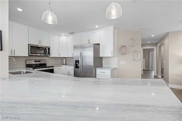 kitchen with light stone counters, sink, decorative light fixtures, white cabinetry, and stainless steel appliances