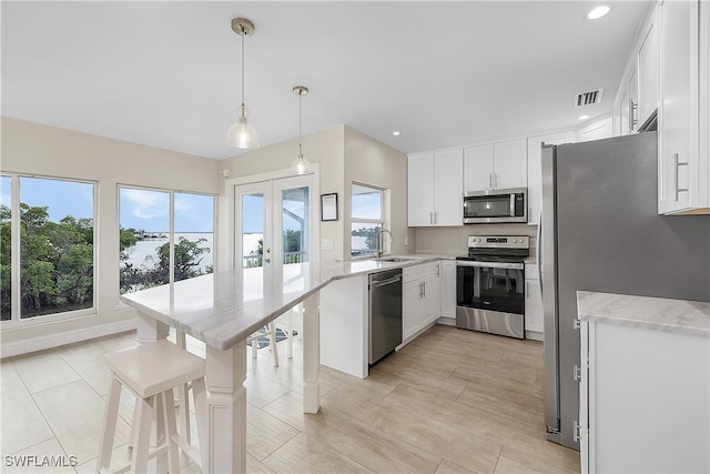 kitchen with pendant lighting, stainless steel appliances, white cabinetry, and plenty of natural light