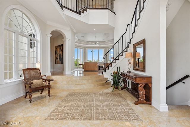 foyer featuring a high ceiling, decorative columns, ceiling fan, and ornamental molding