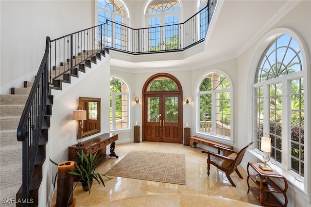 foyer featuring ornamental molding, french doors, a wealth of natural light, and a towering ceiling