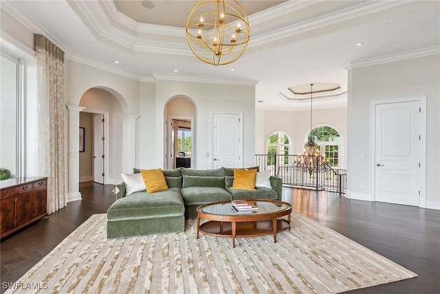 living room featuring ornate columns, dark hardwood / wood-style flooring, a chandelier, ornamental molding, and a raised ceiling