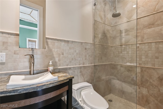 bathroom with toilet, vanity, a tile shower, and tile walls