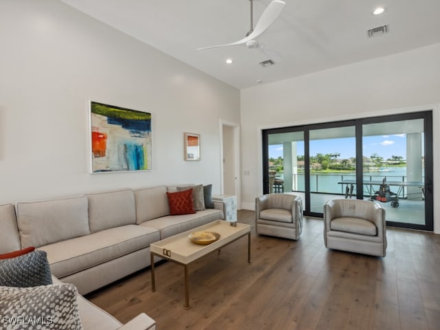 living room with a water view, a towering ceiling, dark hardwood / wood-style flooring, and ceiling fan