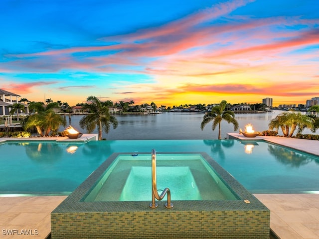 pool at dusk featuring a water view and an in ground hot tub