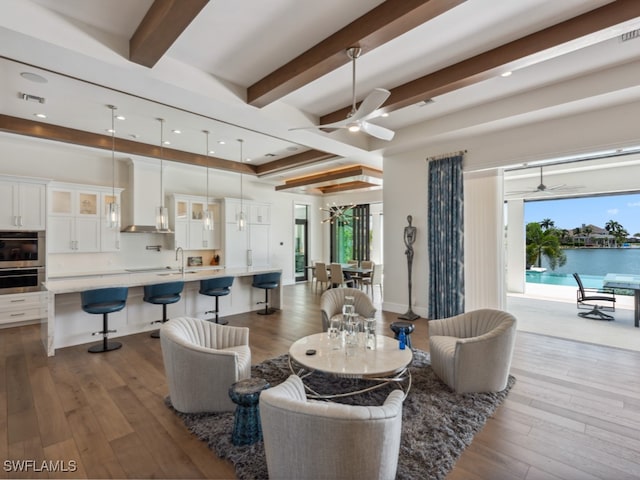 living room featuring ceiling fan, hardwood / wood-style flooring, beam ceiling, and sink