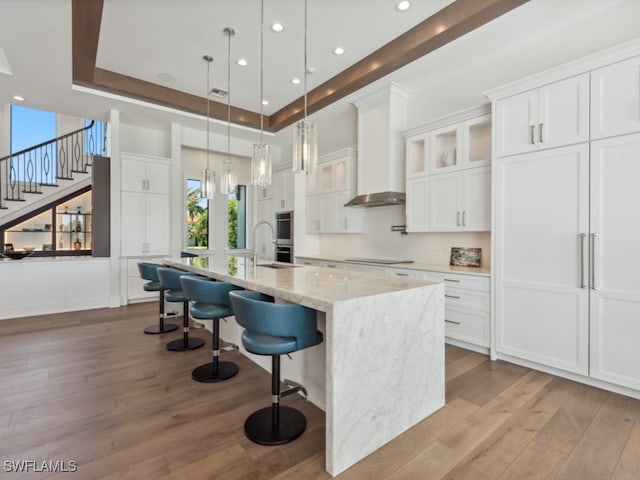 kitchen featuring wood-type flooring, a large island with sink, white cabinetry, black electric cooktop, and light stone countertops