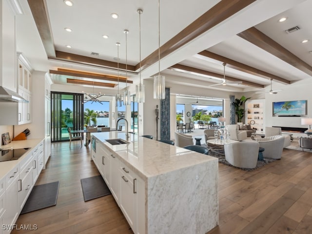 kitchen featuring sink, decorative light fixtures, a large island with sink, white cabinetry, and light stone countertops