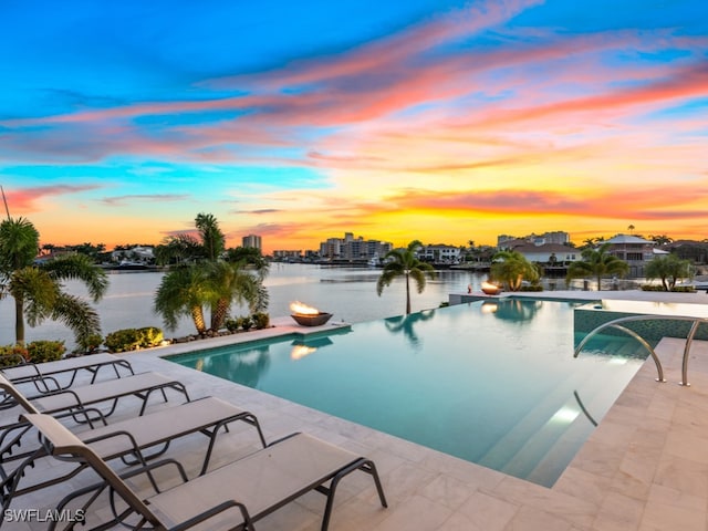 pool at dusk featuring a patio, a water view, and pool water feature