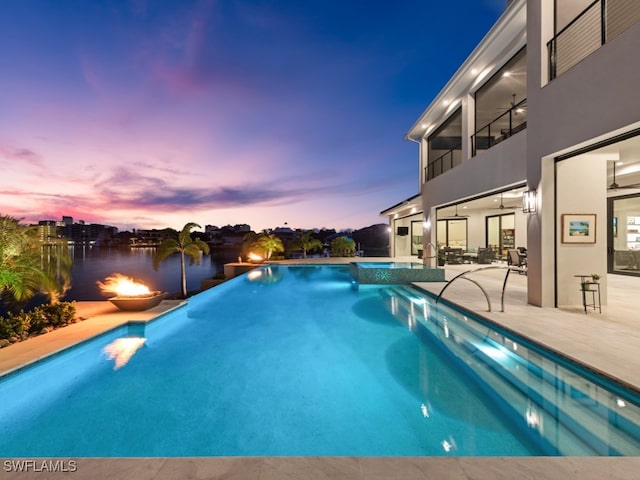 pool at dusk with a water view and a patio area