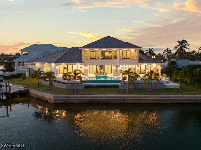 back house at dusk with a yard, a water view, and a patio area