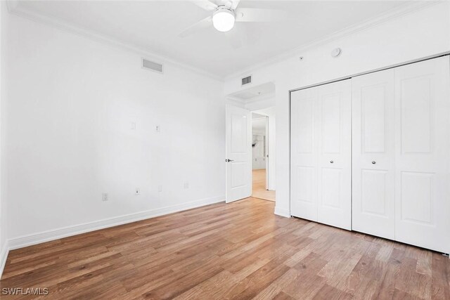 unfurnished bedroom with a closet, crown molding, light hardwood / wood-style floors, and ceiling fan