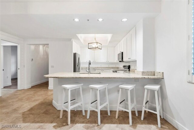 kitchen featuring sink, kitchen peninsula, stainless steel appliances, decorative light fixtures, and white cabinets