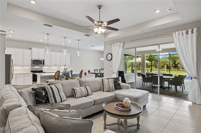 living room featuring ceiling fan, a raised ceiling, and light tile patterned flooring