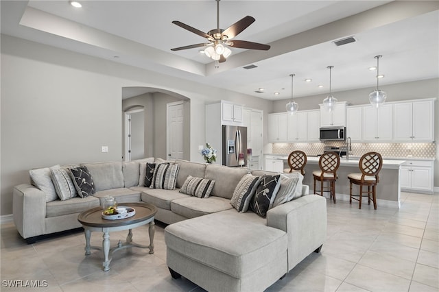 living room with ceiling fan, a tray ceiling, and light tile patterned floors