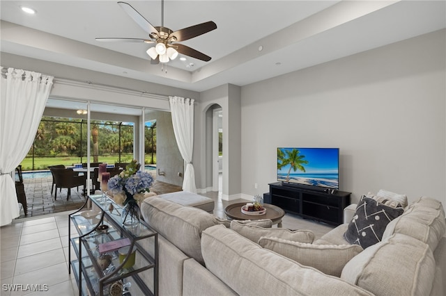 living room featuring light tile patterned floors, a tray ceiling, and ceiling fan