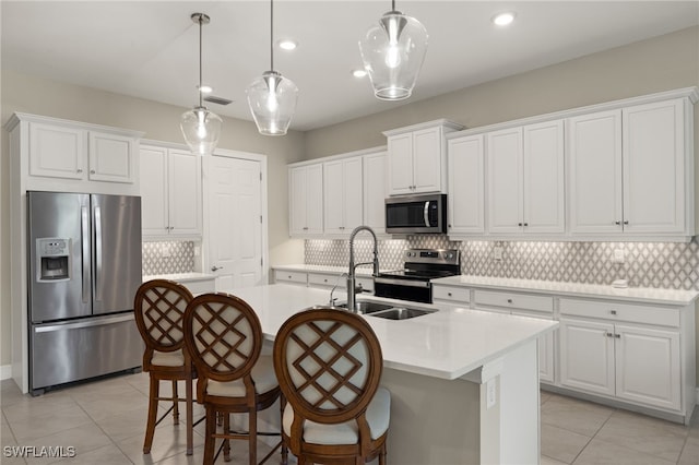 kitchen featuring appliances with stainless steel finishes, white cabinetry, an island with sink, tasteful backsplash, and sink