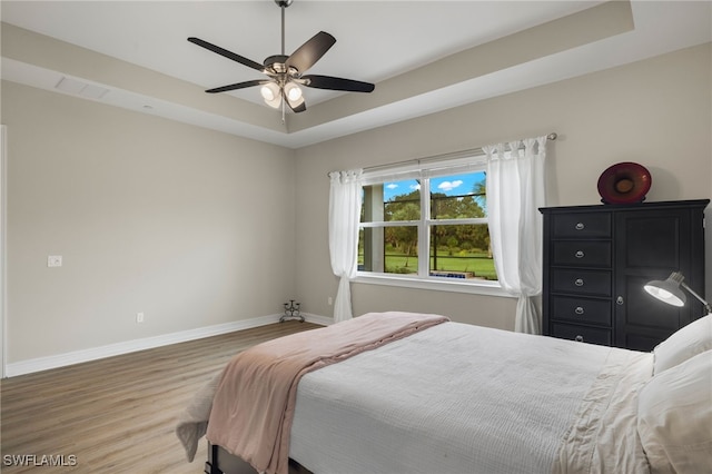 bedroom featuring wood-type flooring, a tray ceiling, and ceiling fan