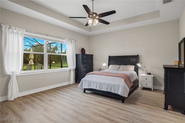 bedroom with ceiling fan, light hardwood / wood-style flooring, and a tray ceiling