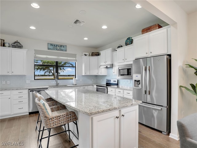 kitchen with light wood-type flooring, stainless steel appliances, sink, white cabinets, and a center island