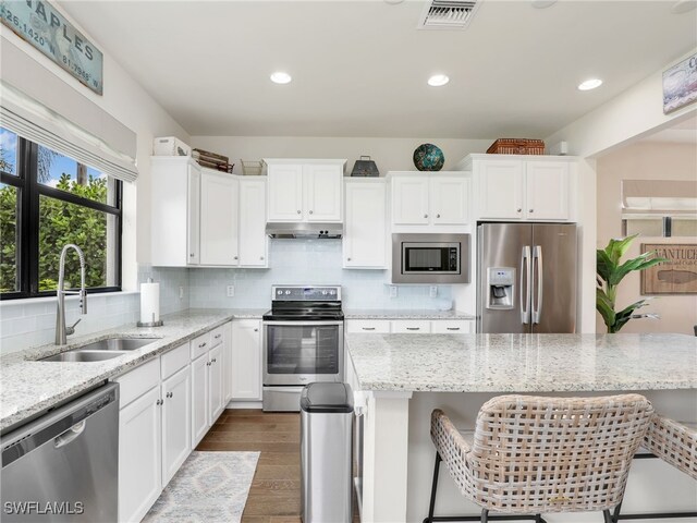 kitchen with a kitchen bar, appliances with stainless steel finishes, light stone countertops, sink, and white cabinets