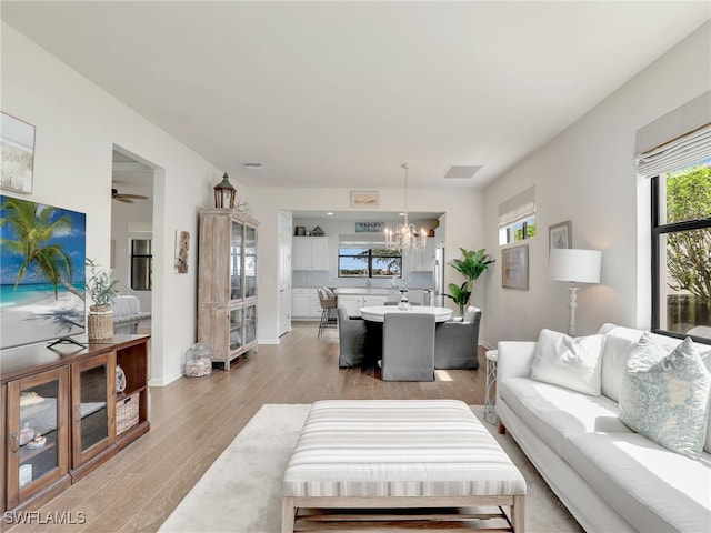 living room with ceiling fan with notable chandelier and light hardwood / wood-style floors