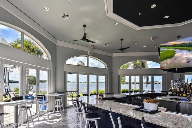 kitchen with ceiling fan, a water view, light stone counters, and french doors