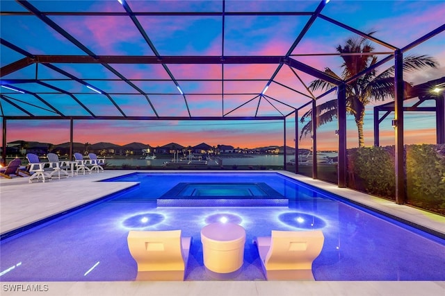 pool at dusk with a patio area, glass enclosure, and an in ground hot tub