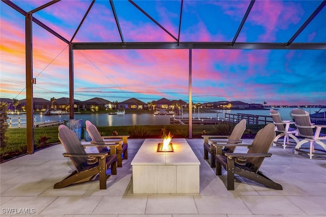 patio terrace at dusk featuring an outdoor fire pit, glass enclosure, and a water view