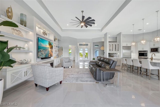 living room featuring sink, french doors, a raised ceiling, and a high ceiling