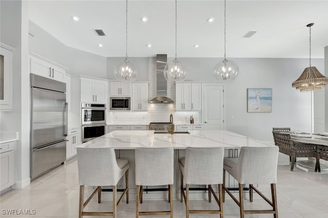 kitchen with built in appliances, pendant lighting, wall chimney exhaust hood, a spacious island, and white cabinets