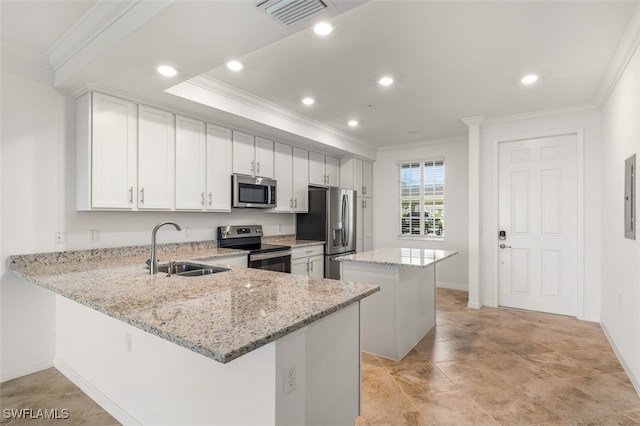 kitchen with appliances with stainless steel finishes, white cabinetry, light stone counters, a kitchen island, and sink